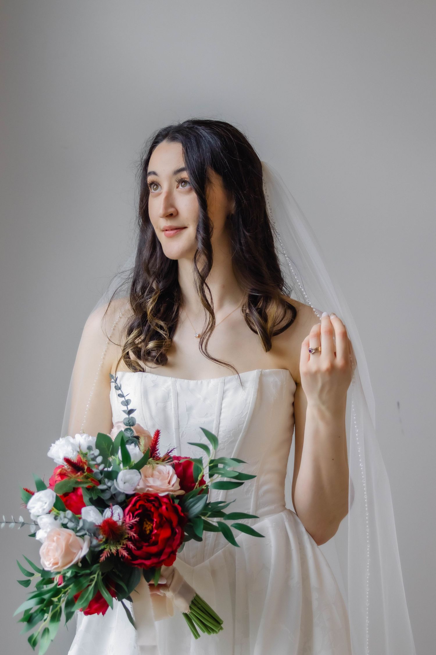 Bridal portrait session with red and pink bouquet against neutral background.