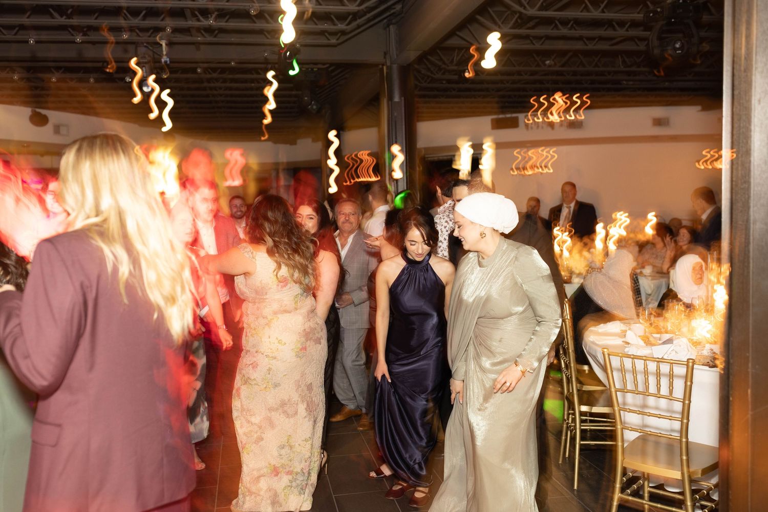 Guests dancing and socializing at an elegant wedding reception with warm lighting and decorated tables.