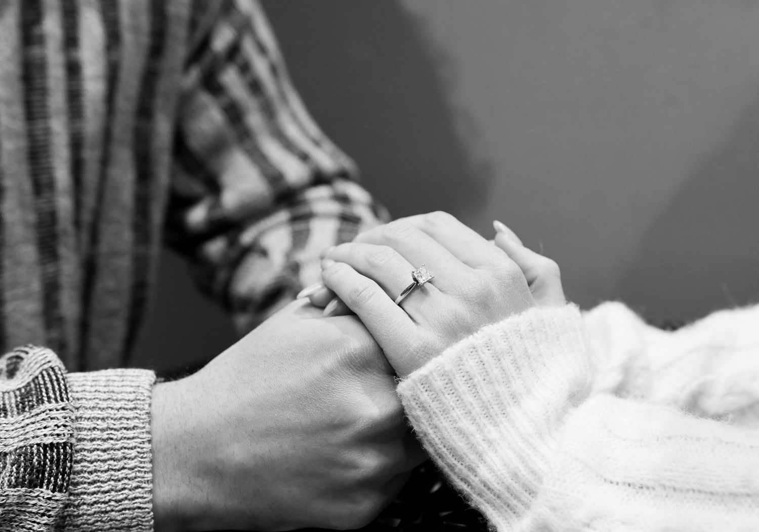 Black and white close-up photo of two hands holding each other, with one hand wearing a ring.
