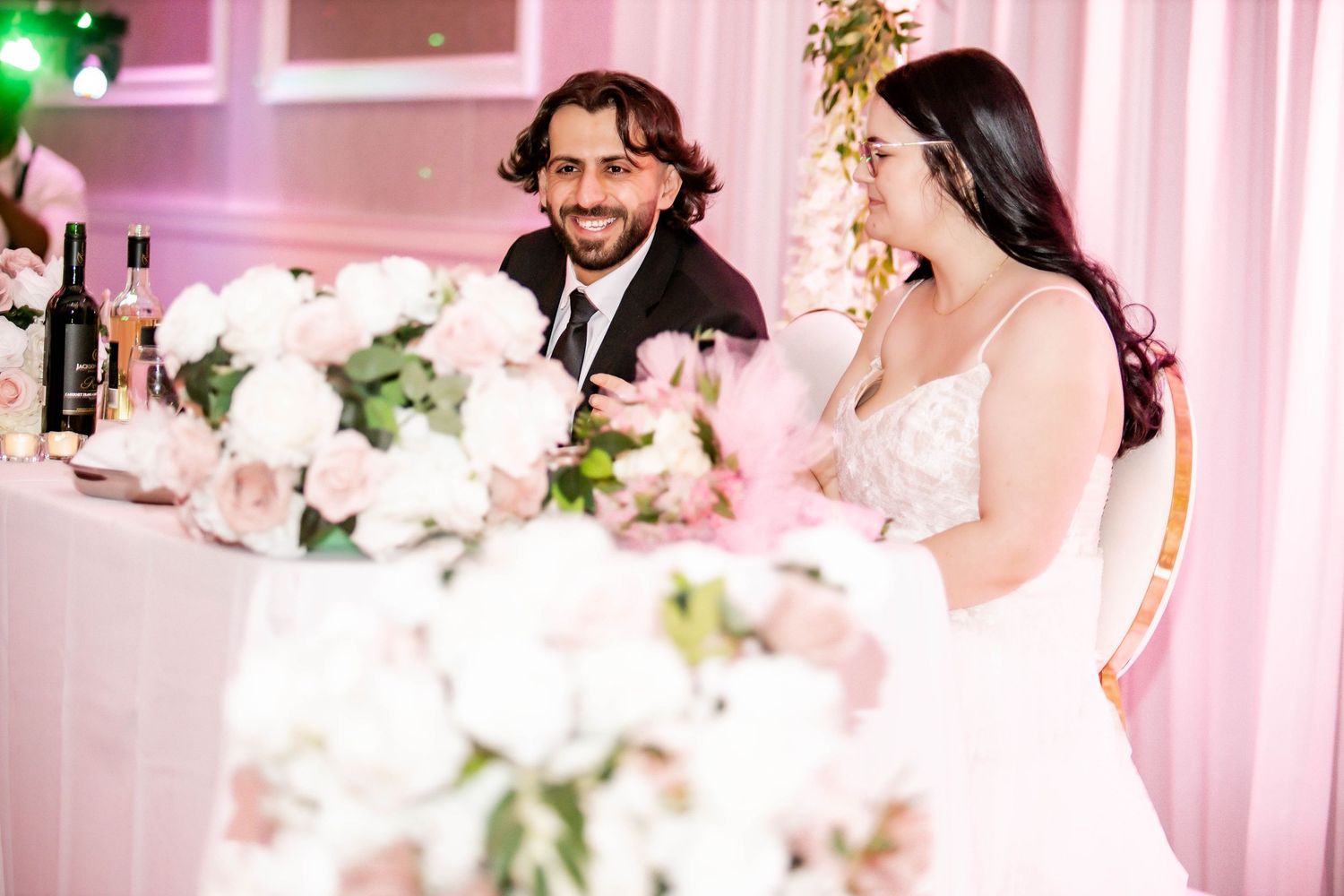 Wedding reception venue decorated with pink lighting and elegant floral arrangements.