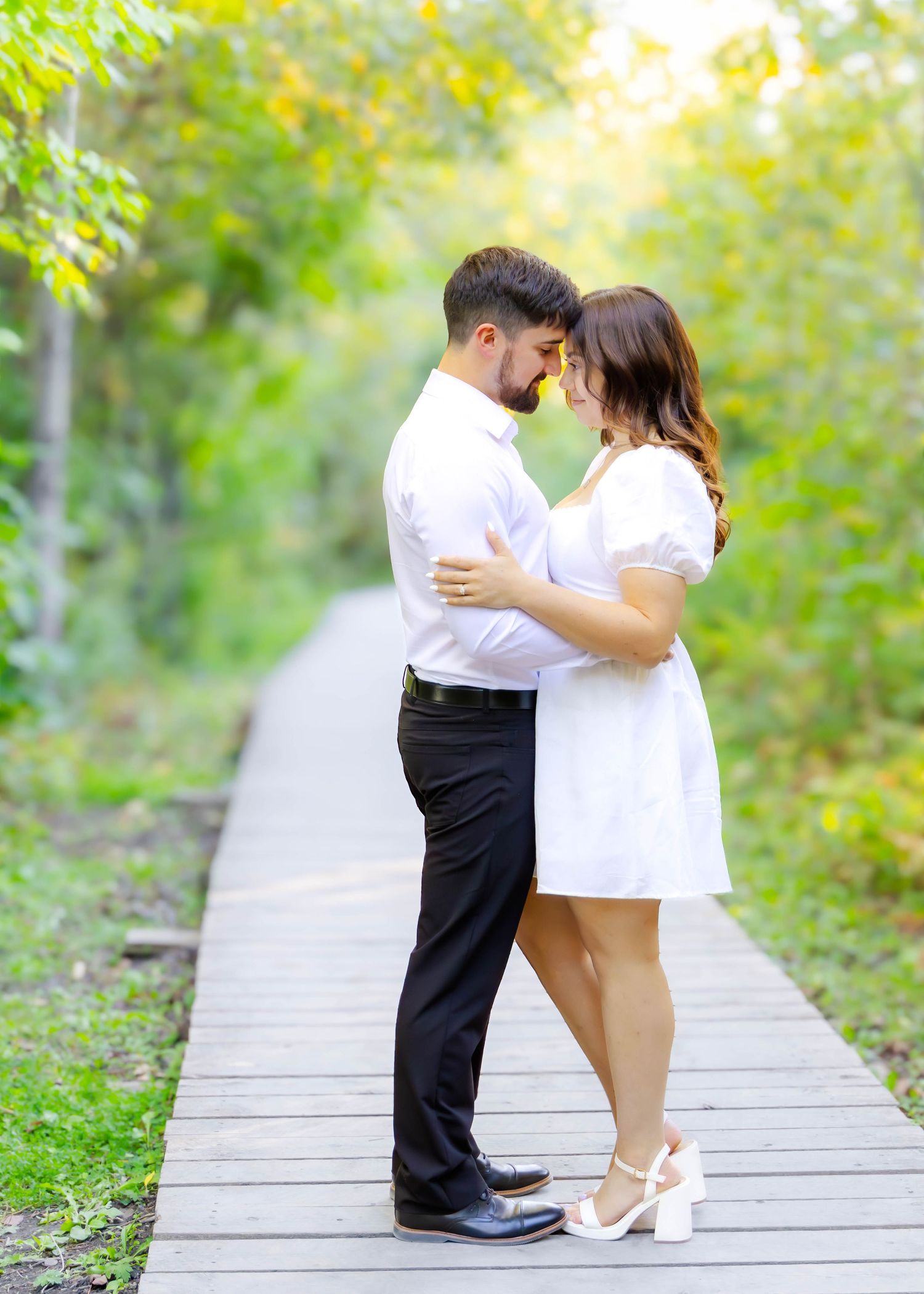 A couple shares a romantic dance on a wooden boardwalk surrounded by lush green foliage.