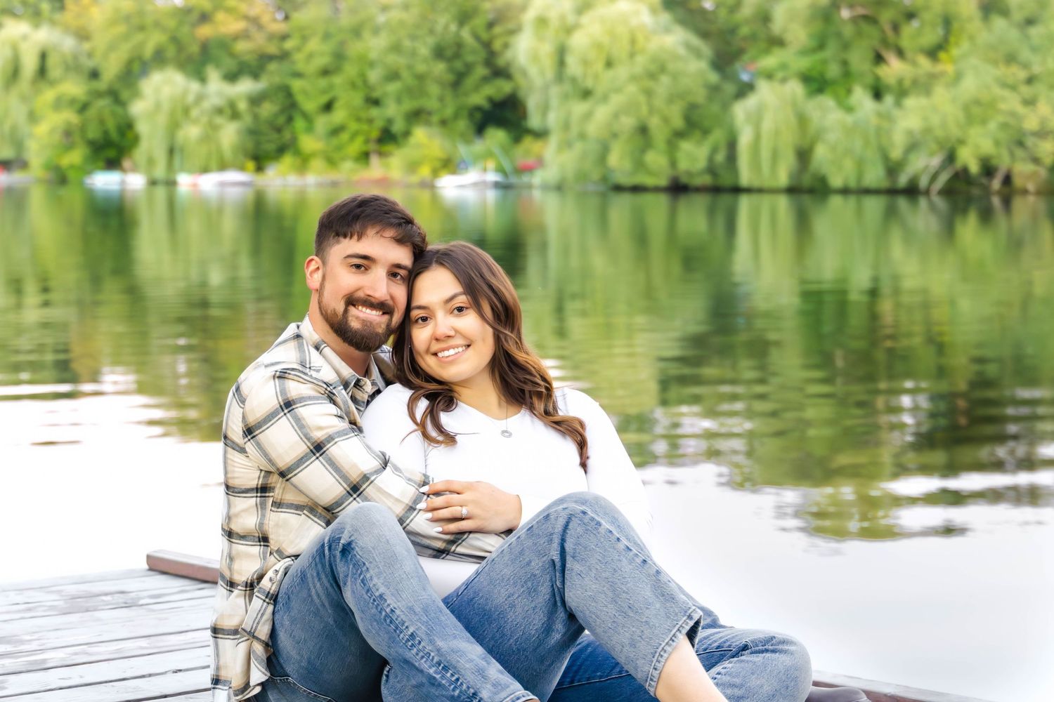 Couple relaxes together on dock with scenic lake and willow trees in background.