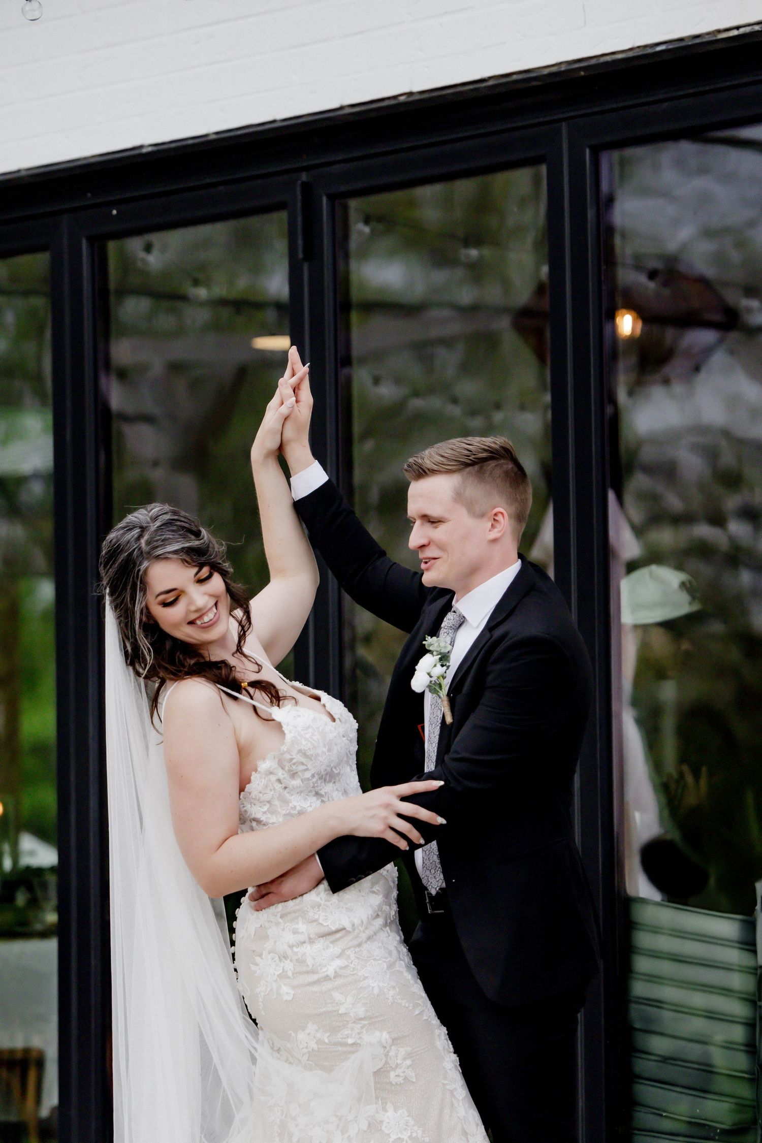 Wedding couple performs a romantic dance move against a modern building exterior.