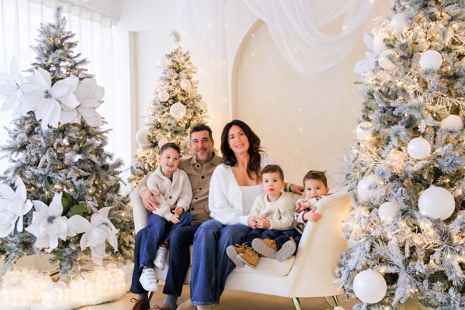 A holiday family portrait with multiple Christmas trees decorated in white and silver themes.