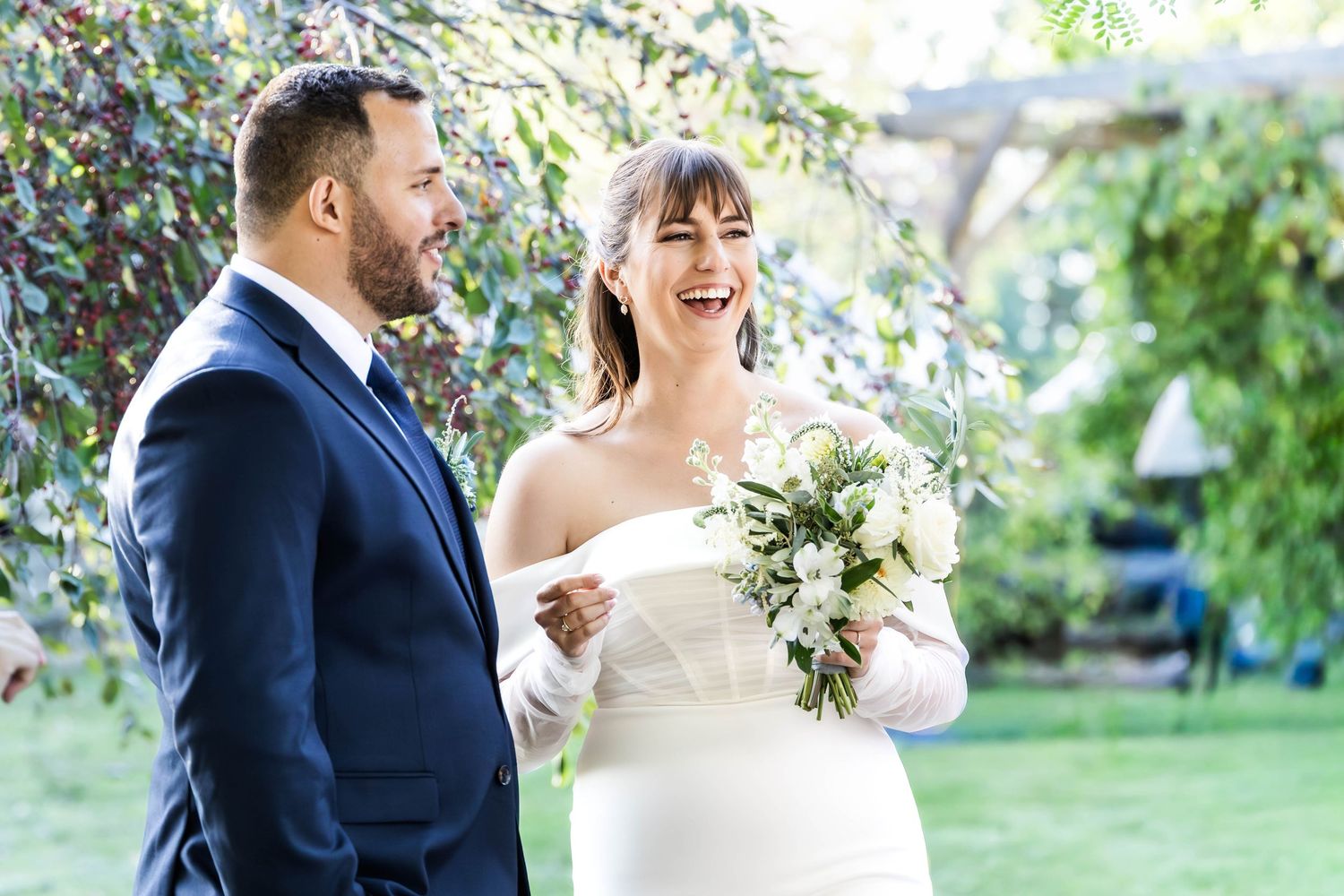 A happy couple shares a joyful moment together outdoors in a garden setting during a wedding celebration.