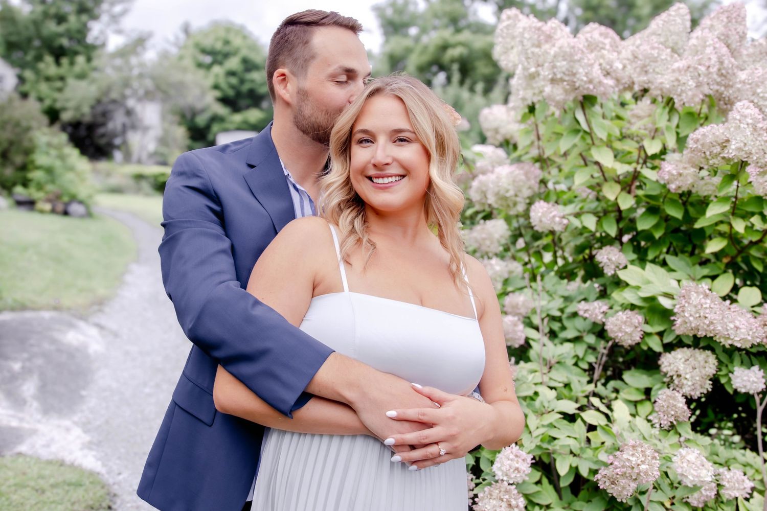 A romantic outdoor photo session in a lush garden with blooming pink lilac bushes and natural greenery.