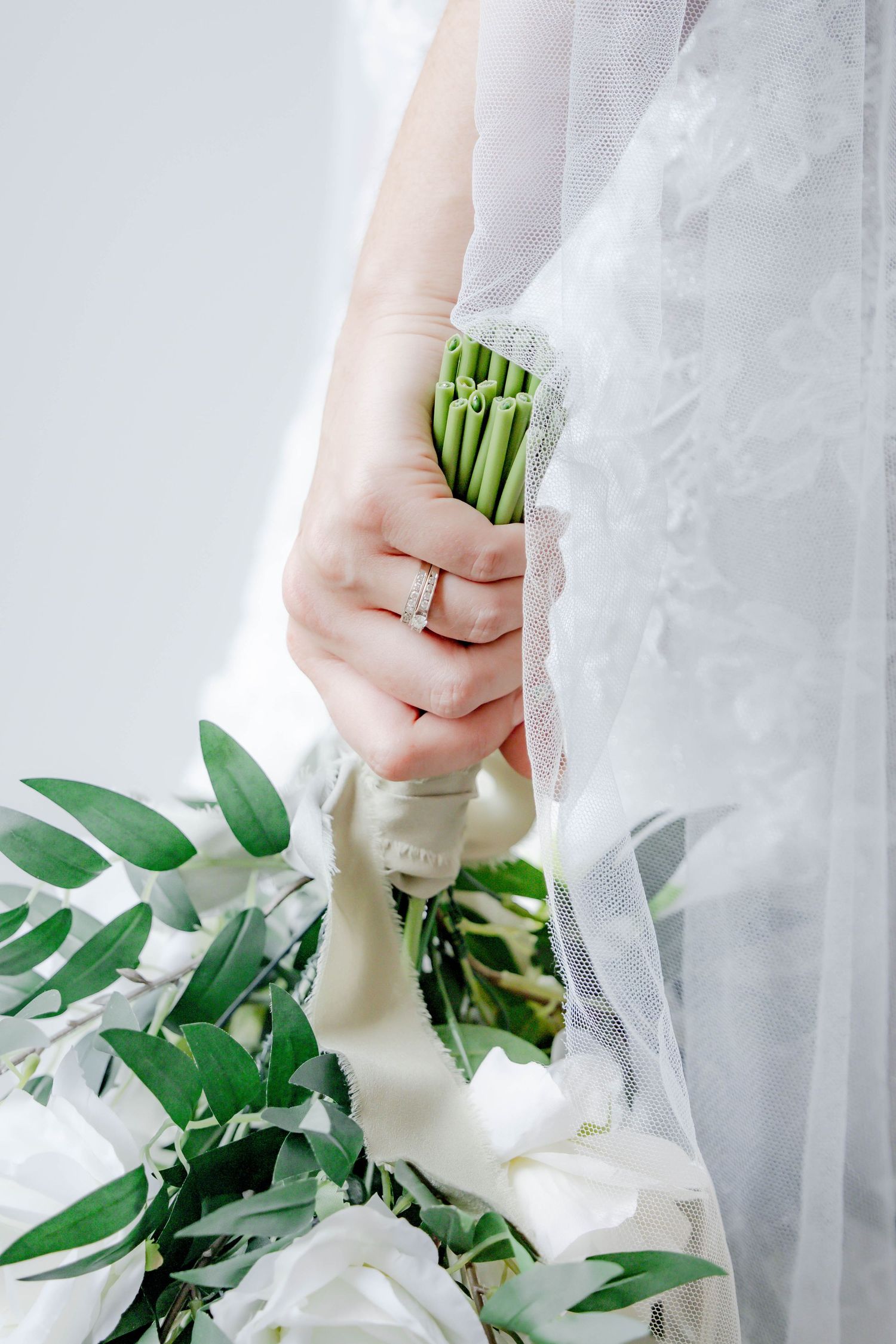Close-up of white wedding dress details and bridal bouquet with fresh greenery and white flowers.