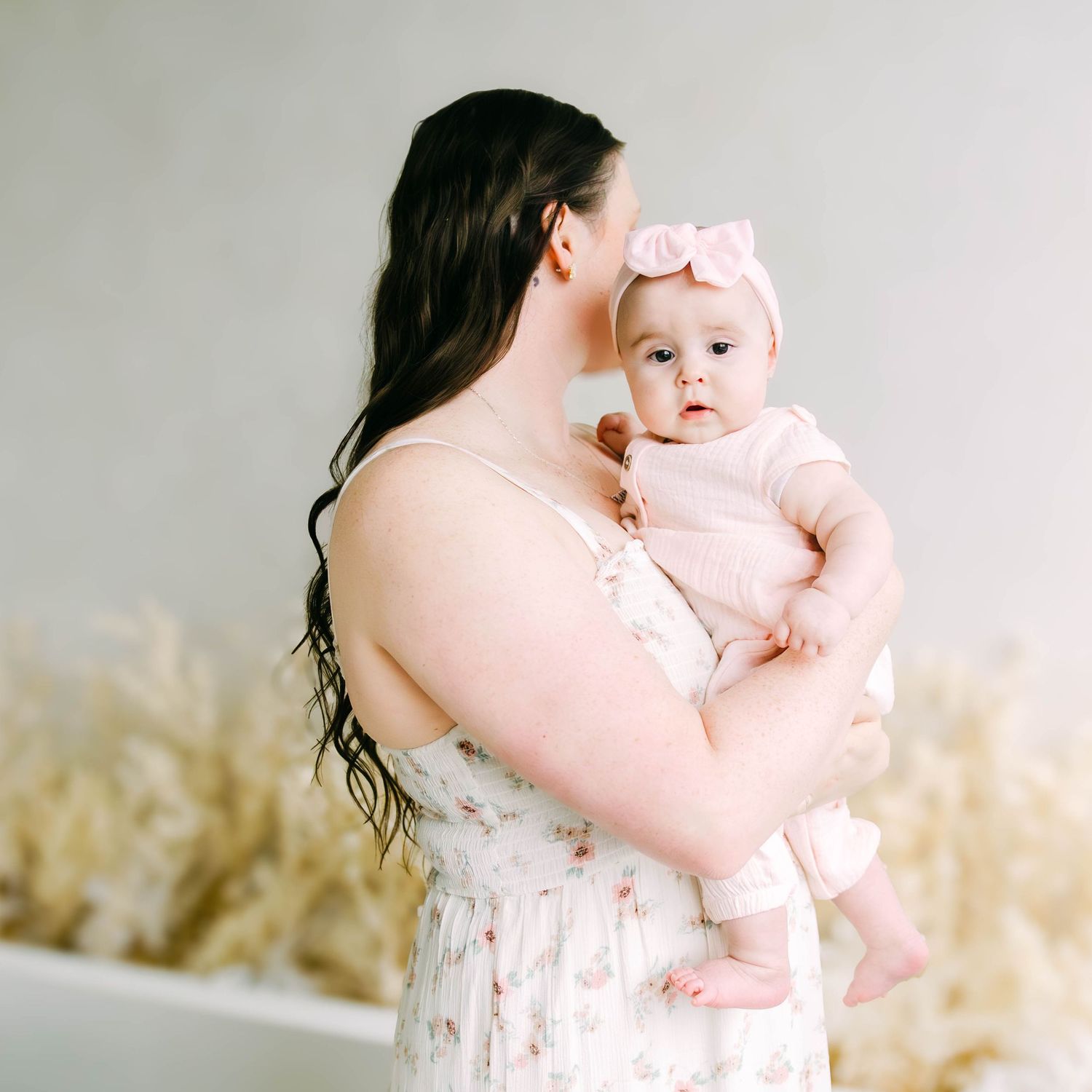 Tender moments captured between parent and infant in delicate pink clothing against neutral background.