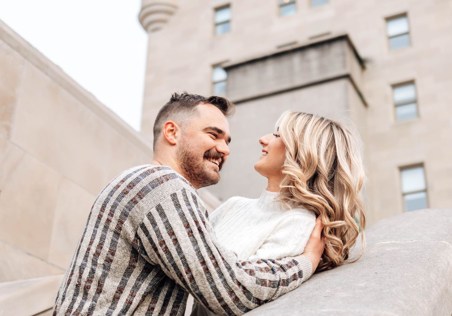 A couple shares a romantic moment together outside a beige stone building on a sunny day.