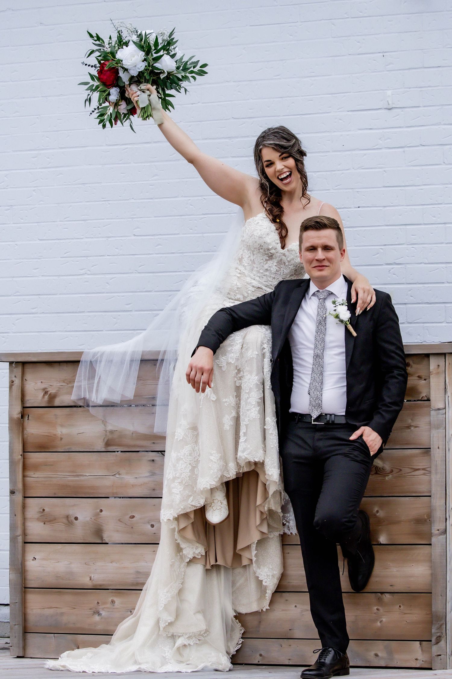 Playful wedding couple posing together against a rustic wooden wall backdrop.