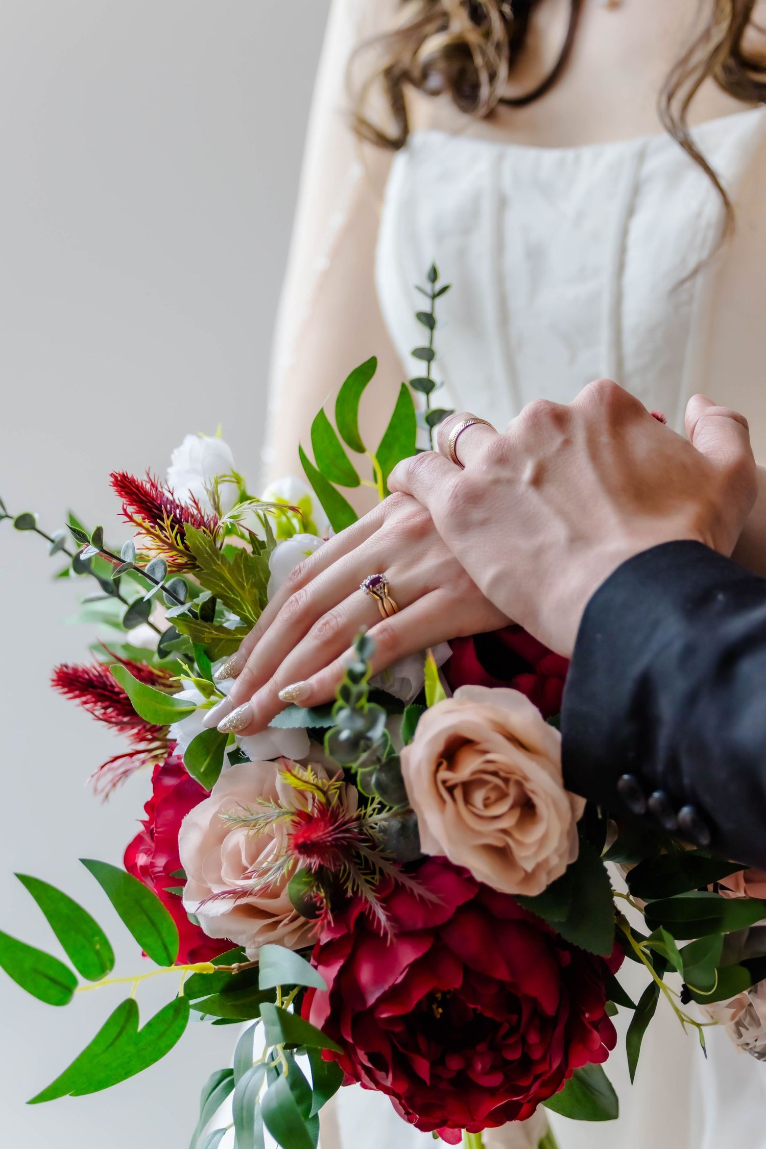 Elegant bridal bouquet featuring deep red and blush roses with mixed greenery held against a white dress.