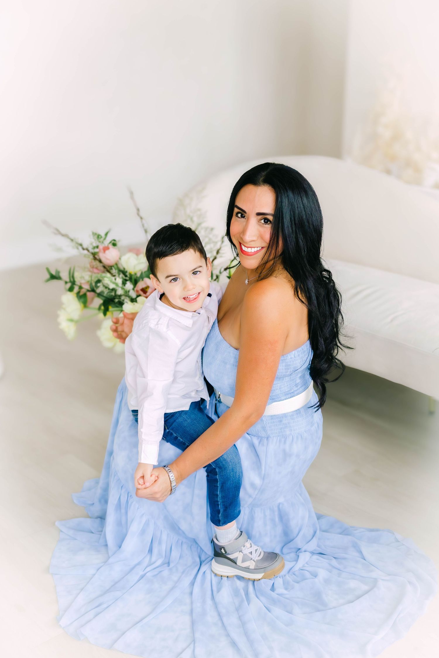Mother and child in matching blue and white outfits pose in bright studio setting.