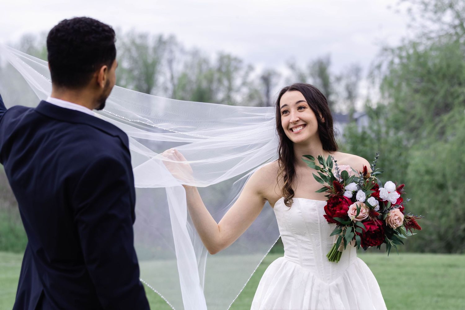 Bride and groom share romantic moments outdoors as her long white veil flows in the wind.