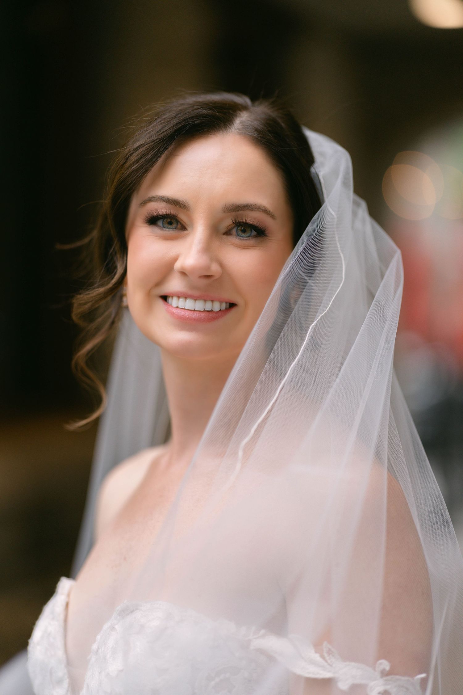 Beautiful bride smiling softly wearing a flowing white veil and lace wedding dress on her wedding day.
