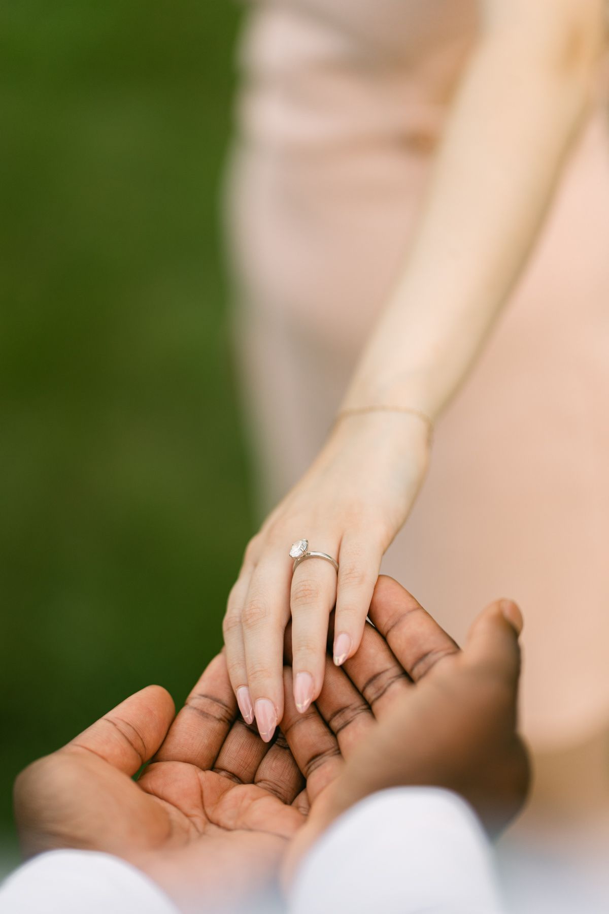 Close-up of an interracial couple holding hands, woman wearing a diamond engagement ring on her finger.