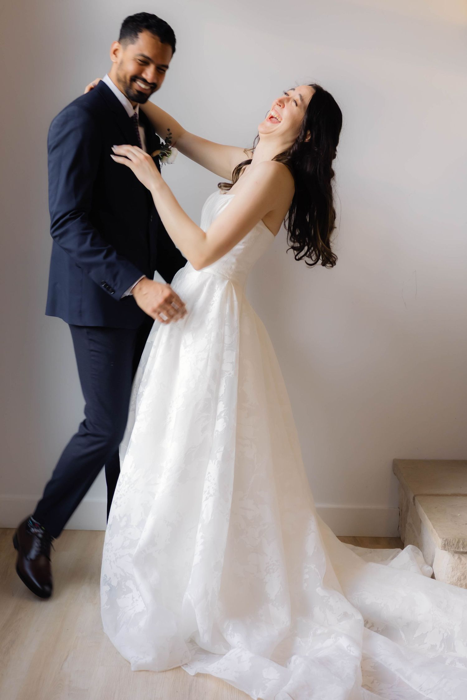 Couple dancing and laughing together in a sunlit room with white walls.