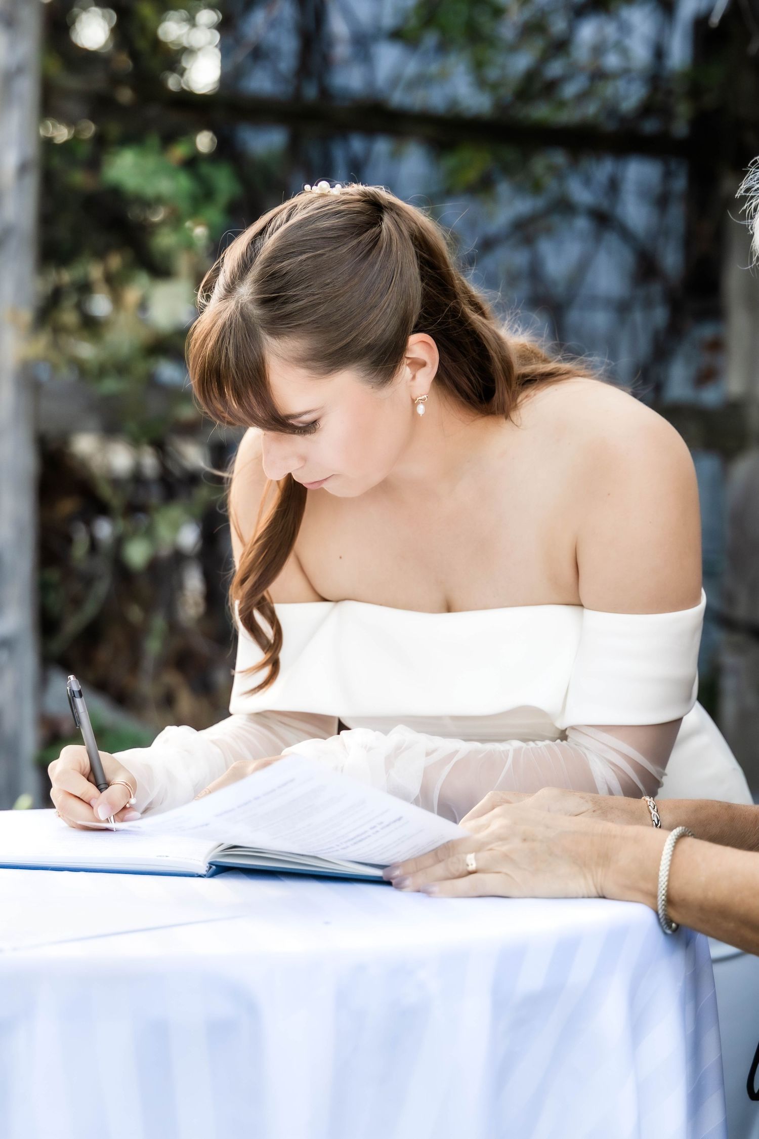 Student in white off-shoulder top writes in notebook while studying at desk near window.