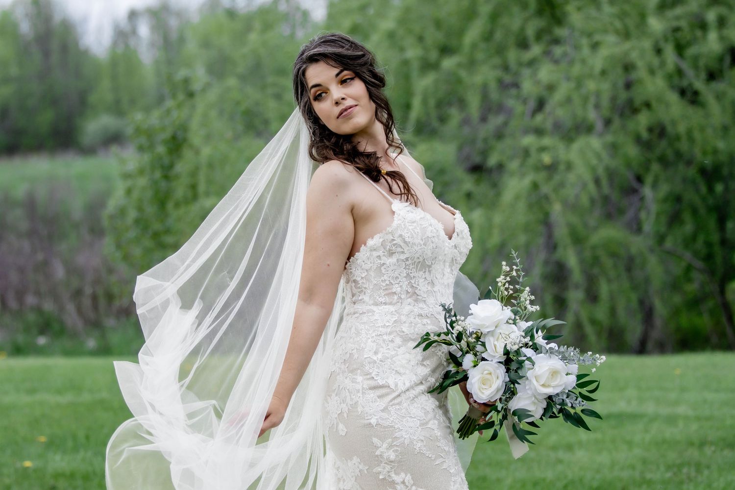 Flowing white wedding dress with lace details in a natural outdoor setting.