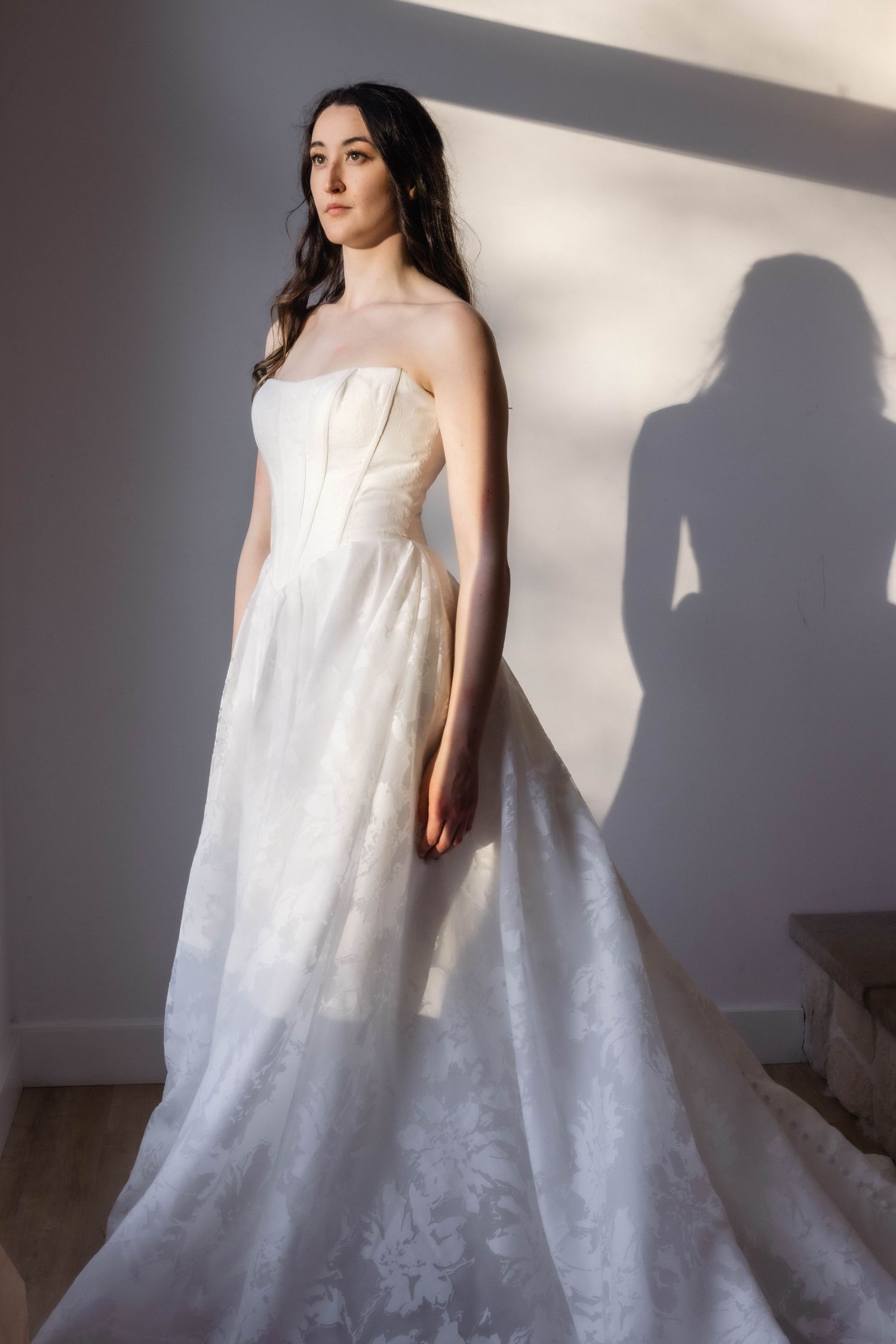 Elegant strapless wedding gown with textured floral pattern and dramatic train in natural lighting.
