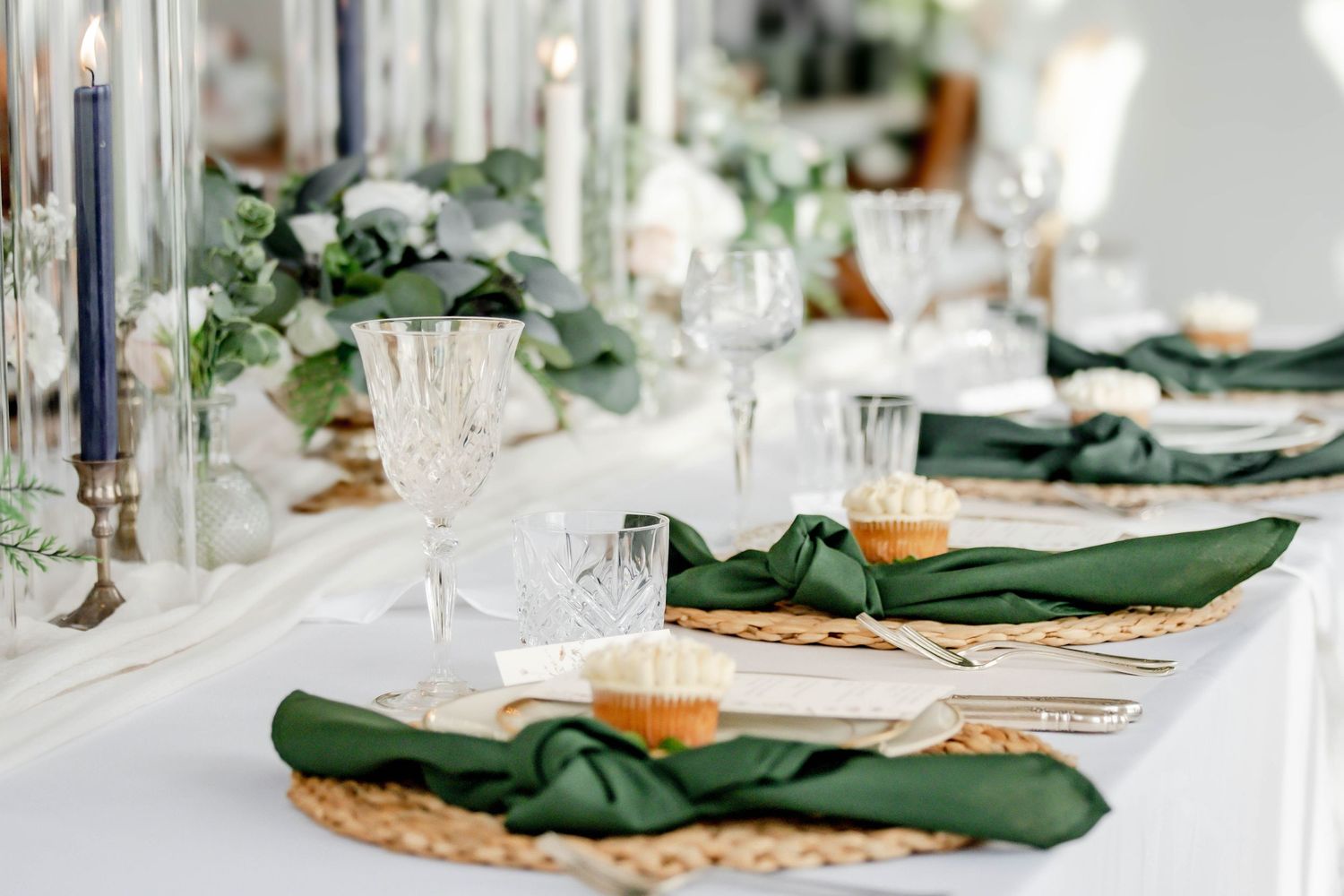 Elegant wedding reception table setting with green napkins, white florals and crystal glassware.