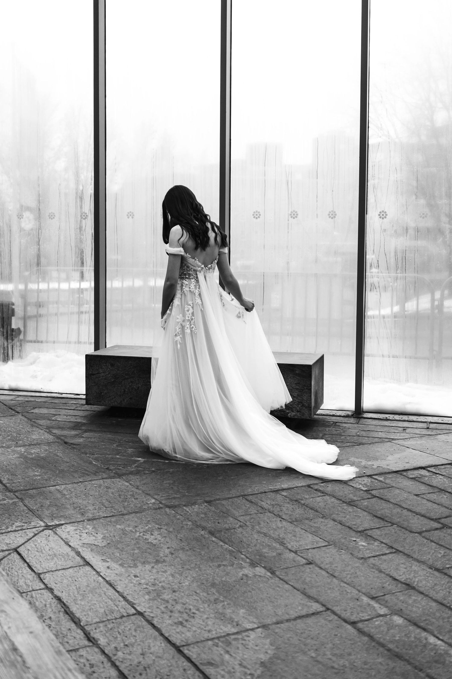 A black and white photo series showing a flowing white wedding dress moving across a concrete floor in a windowed space.