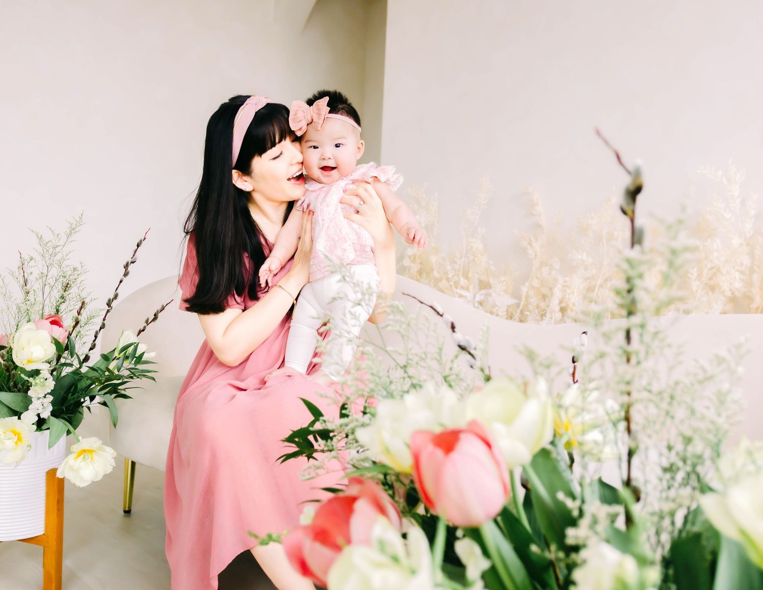 A person in pink clothing poses with white and pink flowers in a bright, sunlit setting.