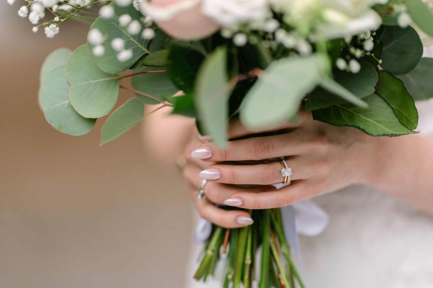 Bride holding a wedding bouquet of roses and eucalyptus, showcasing a sparkling diamond engagement ring on her finger.