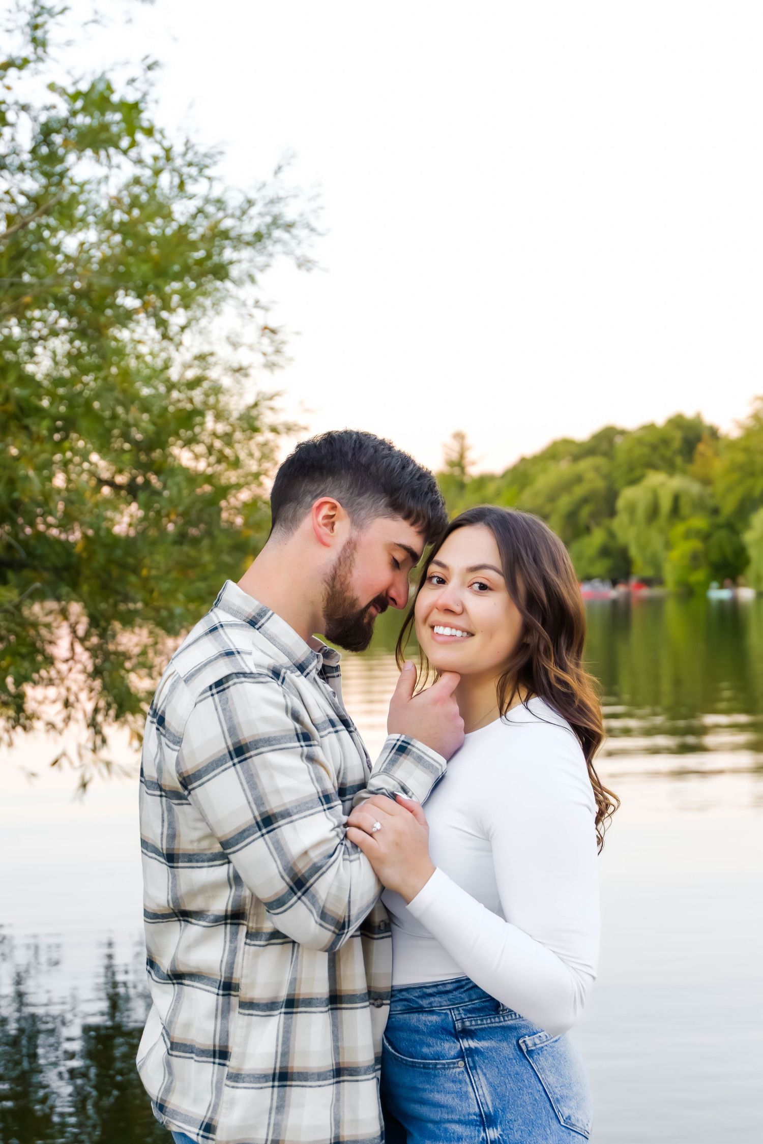 Couple in plaid and white share intimate moment by scenic lake at sunset.