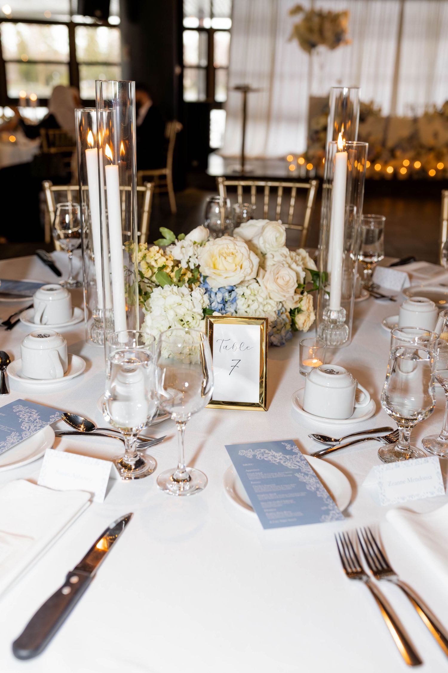 Elegant wedding reception table set with candles, blue hydrangea centerpiece, and blue menus.