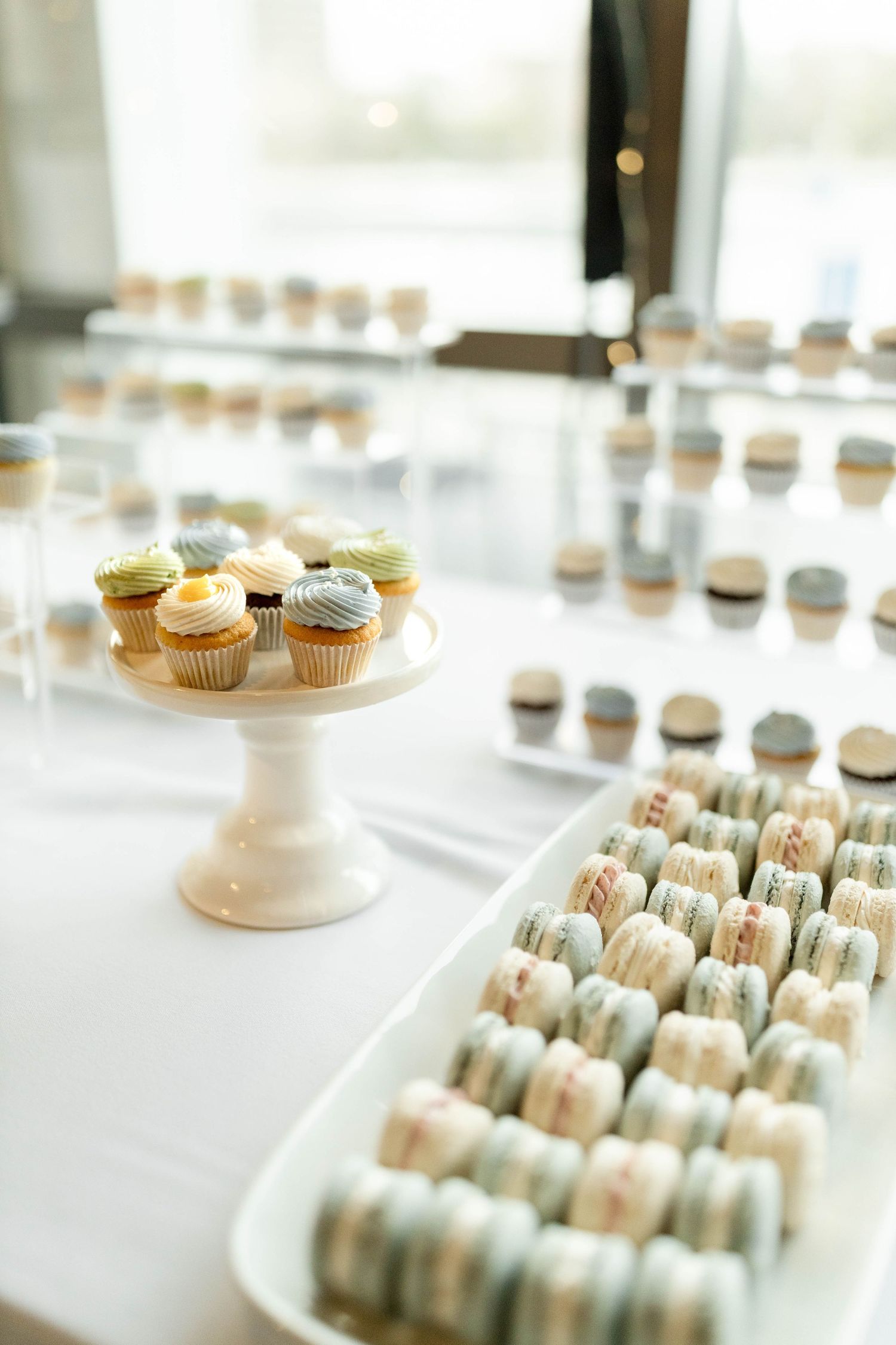 Elegant wedding dessert table with pastel cupcakes on a white cake stand and rows of macarons on a white platter.