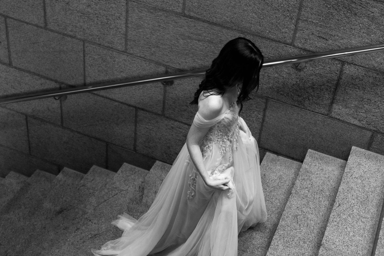 Black and white photo of a bride in a flowing white wedding dress descending stone stairs.