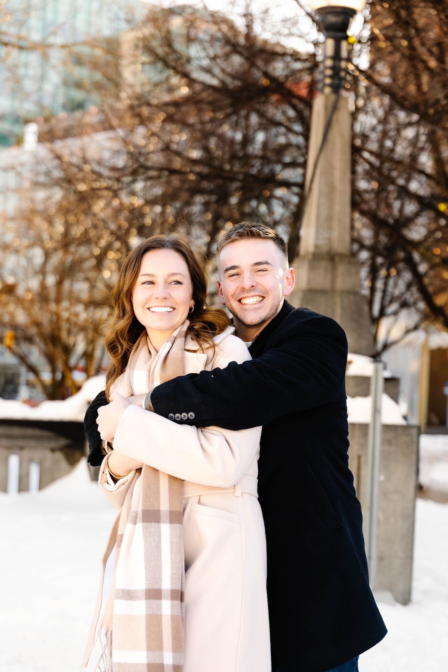 A couple shares joyful laughter together in a winter setting with snow-covered trees in the background.
