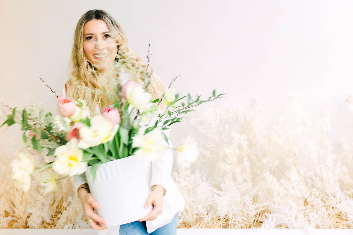 Person holding white vase with fresh spring flowers against textured cream background.
