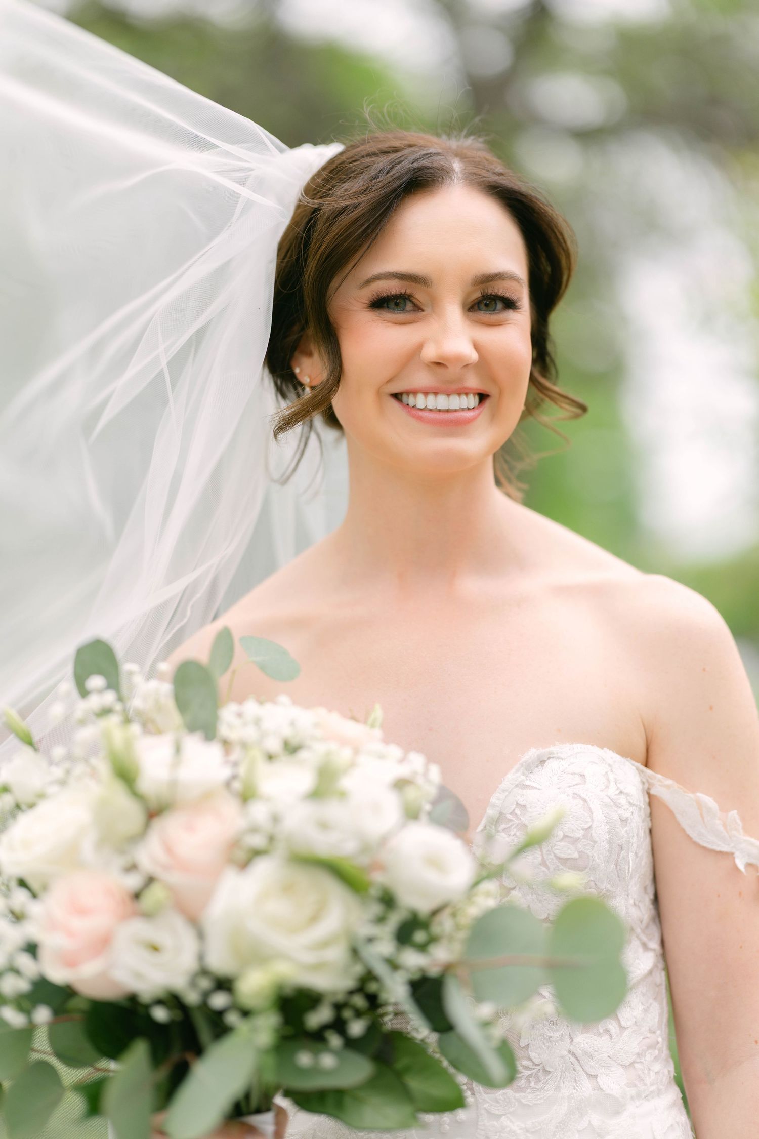 Beautiful bride smiling with veil flowing, holding blush and white rose bouquet with eucalyptus.