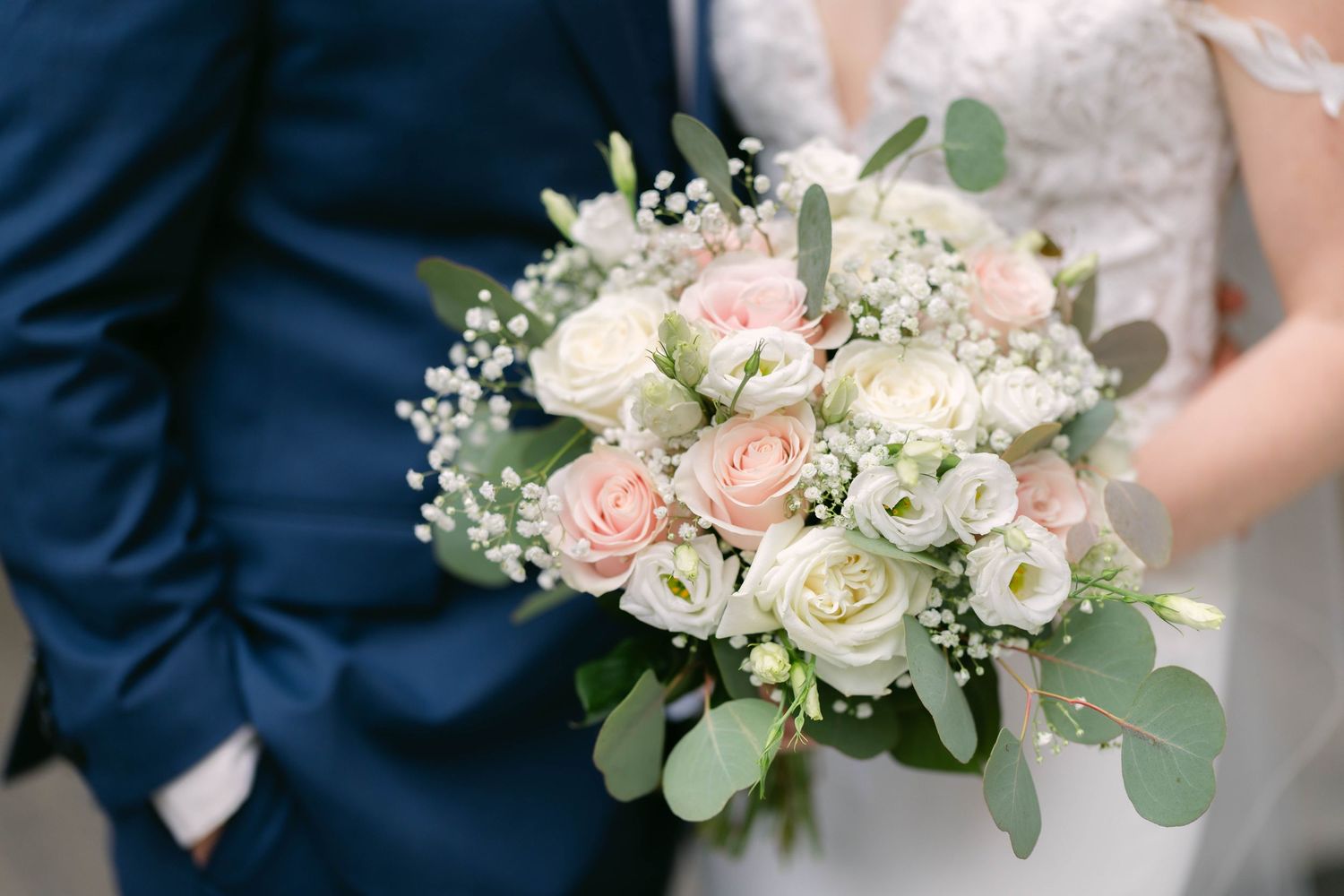 Bride and groom holding a elegant wedding bouquet of pink roses, white flowers, and eucalyptus greenery.