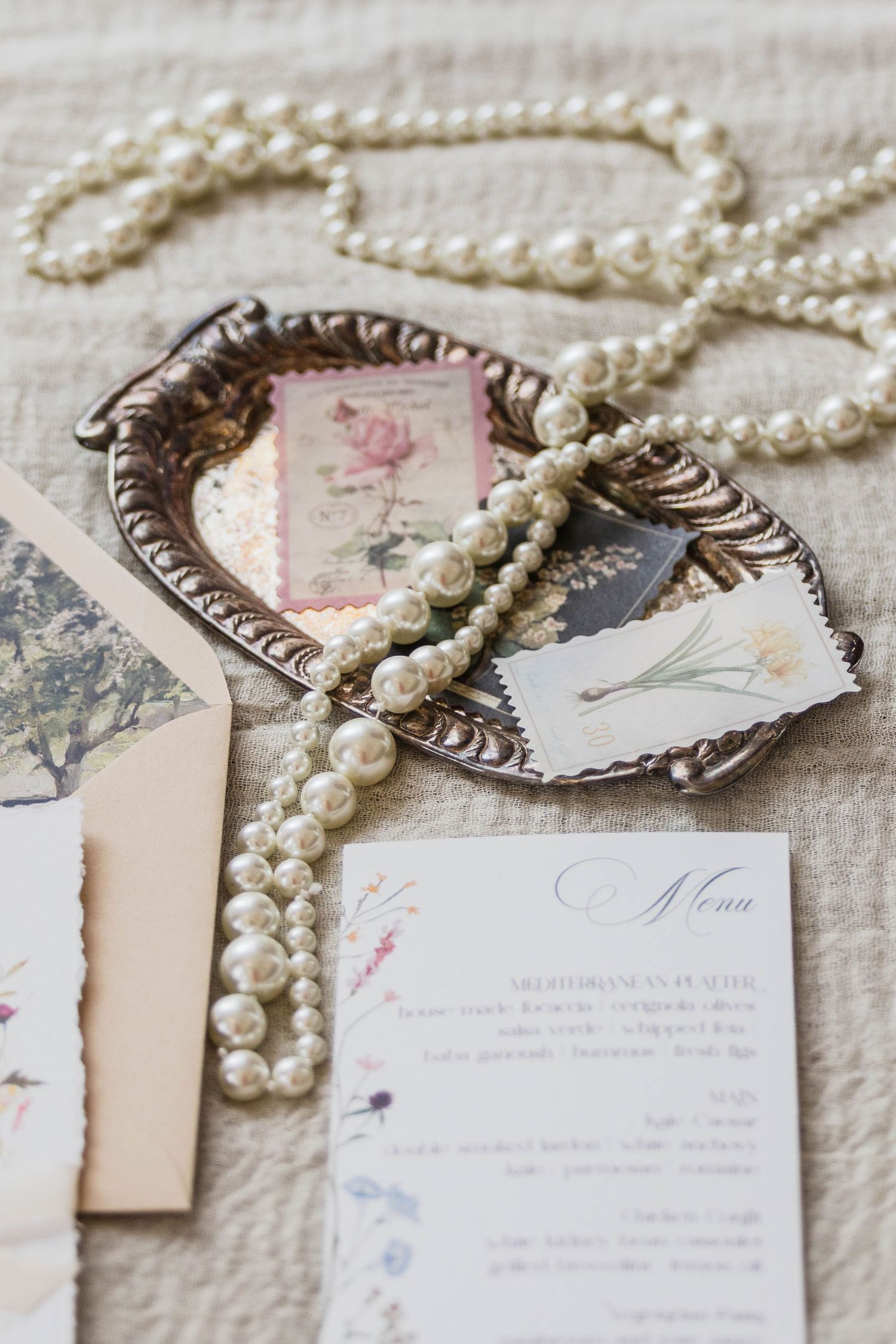 Vintage wedding invitations with delicate pearl necklaces and romantic floral details arranged on a textured cream surface.