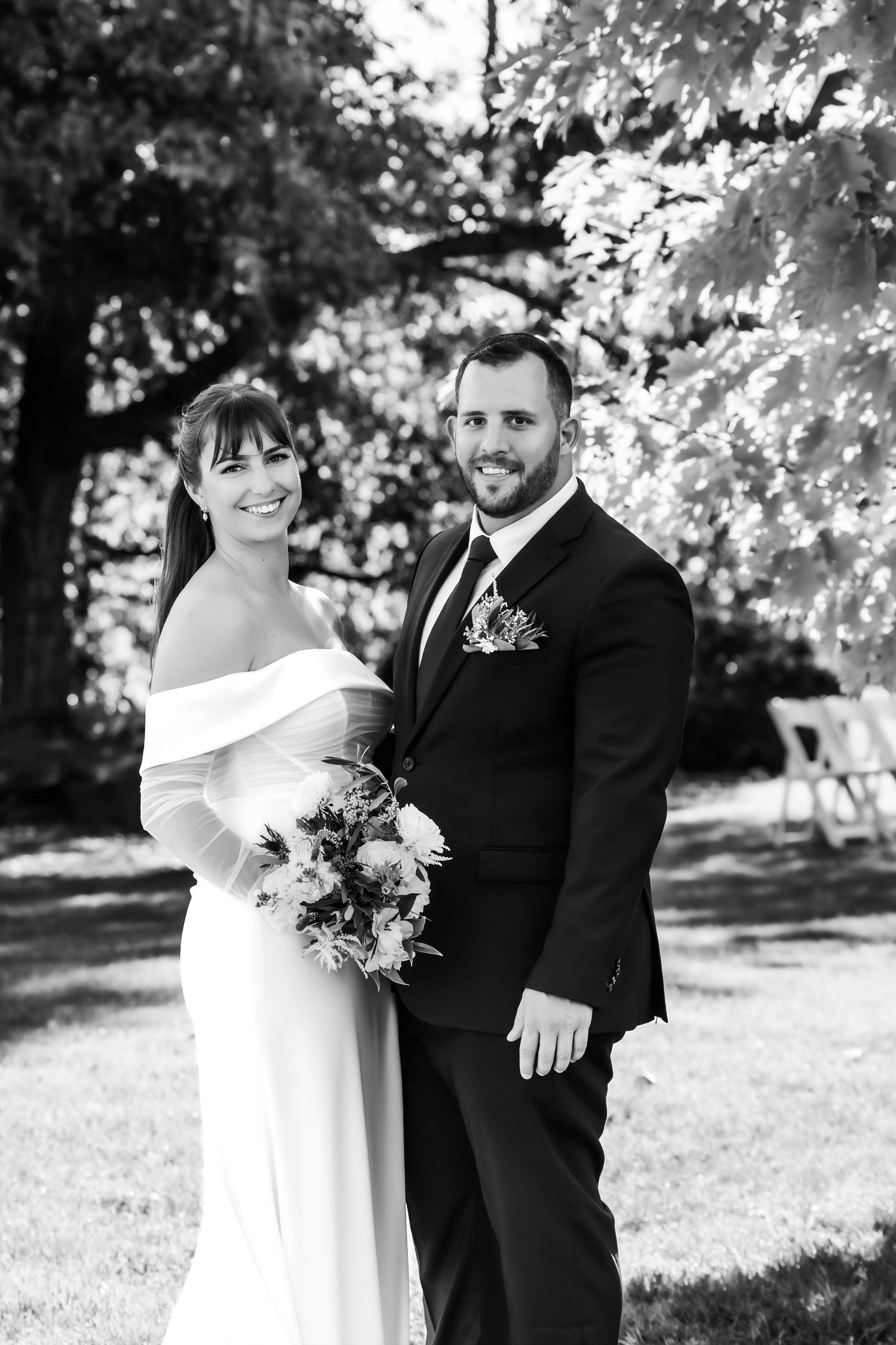 A black and white wedding photo series showing a couple in formal attire posing outdoors with flowers.