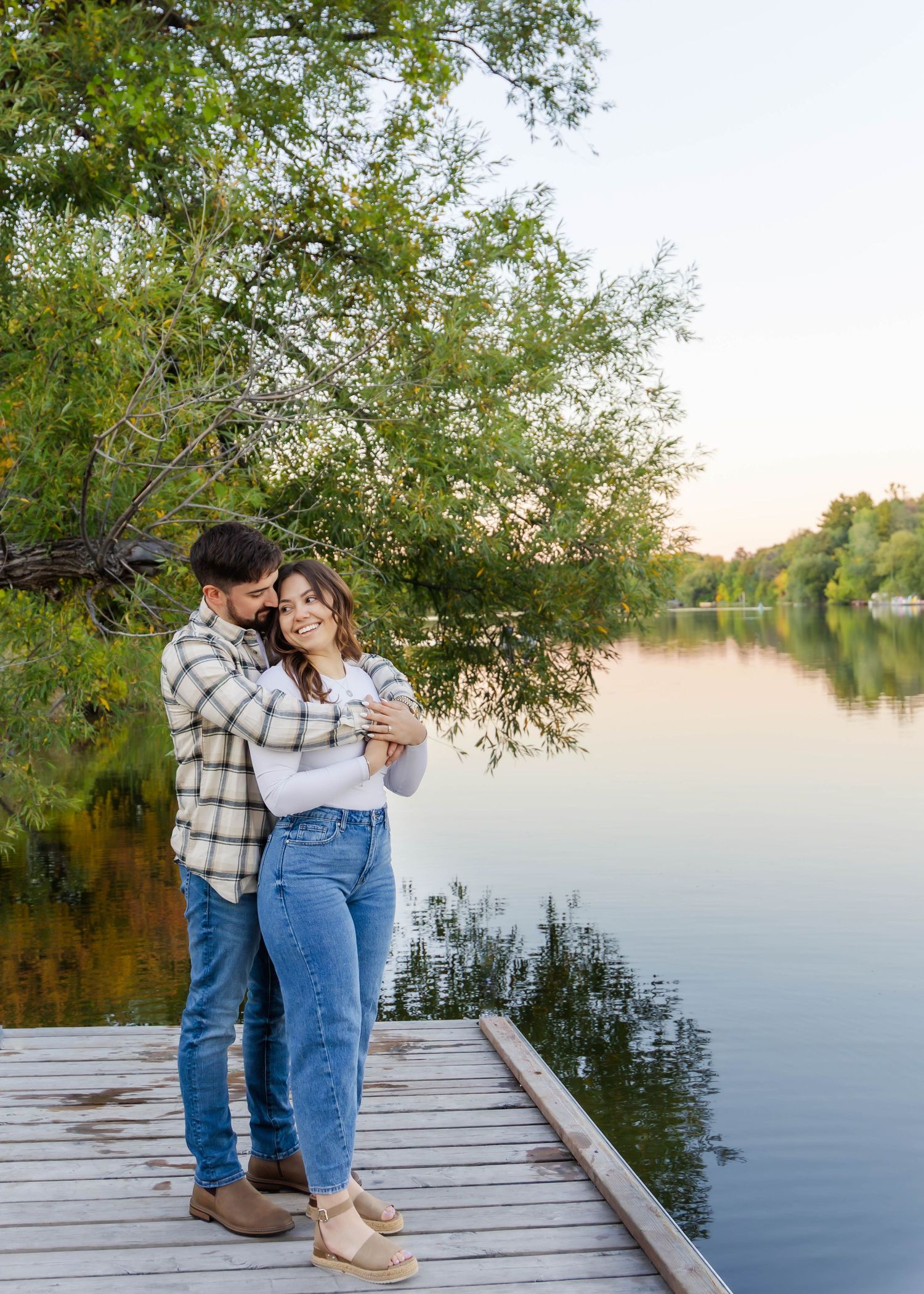 Couple sharing tender moment on wooden dock with serene lake view at sunset.