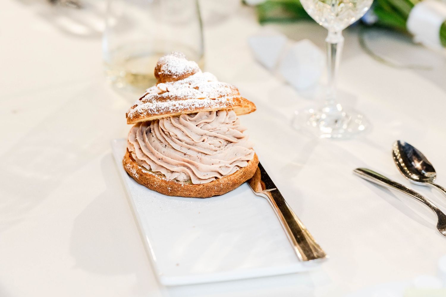 Elegant cream puff pastry dessert dusted with powdered sugar served on a marble plate at a wedding reception.