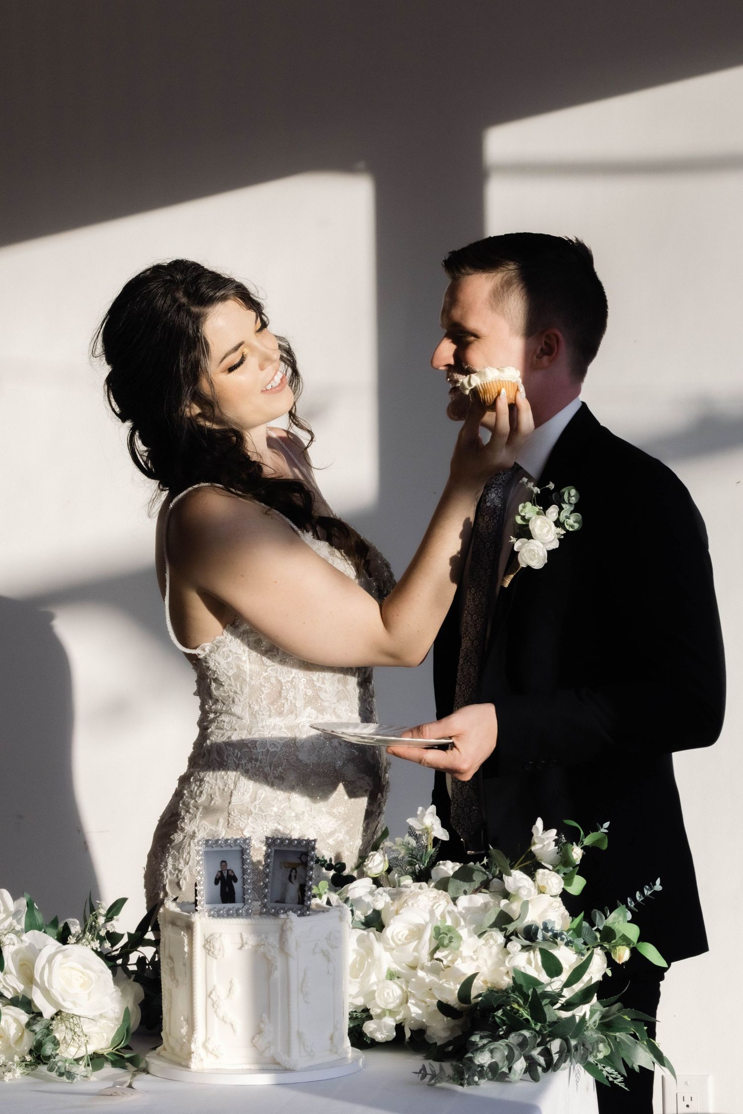 Playful cake feeding moment captured during wedding reception with dramatic lighting.