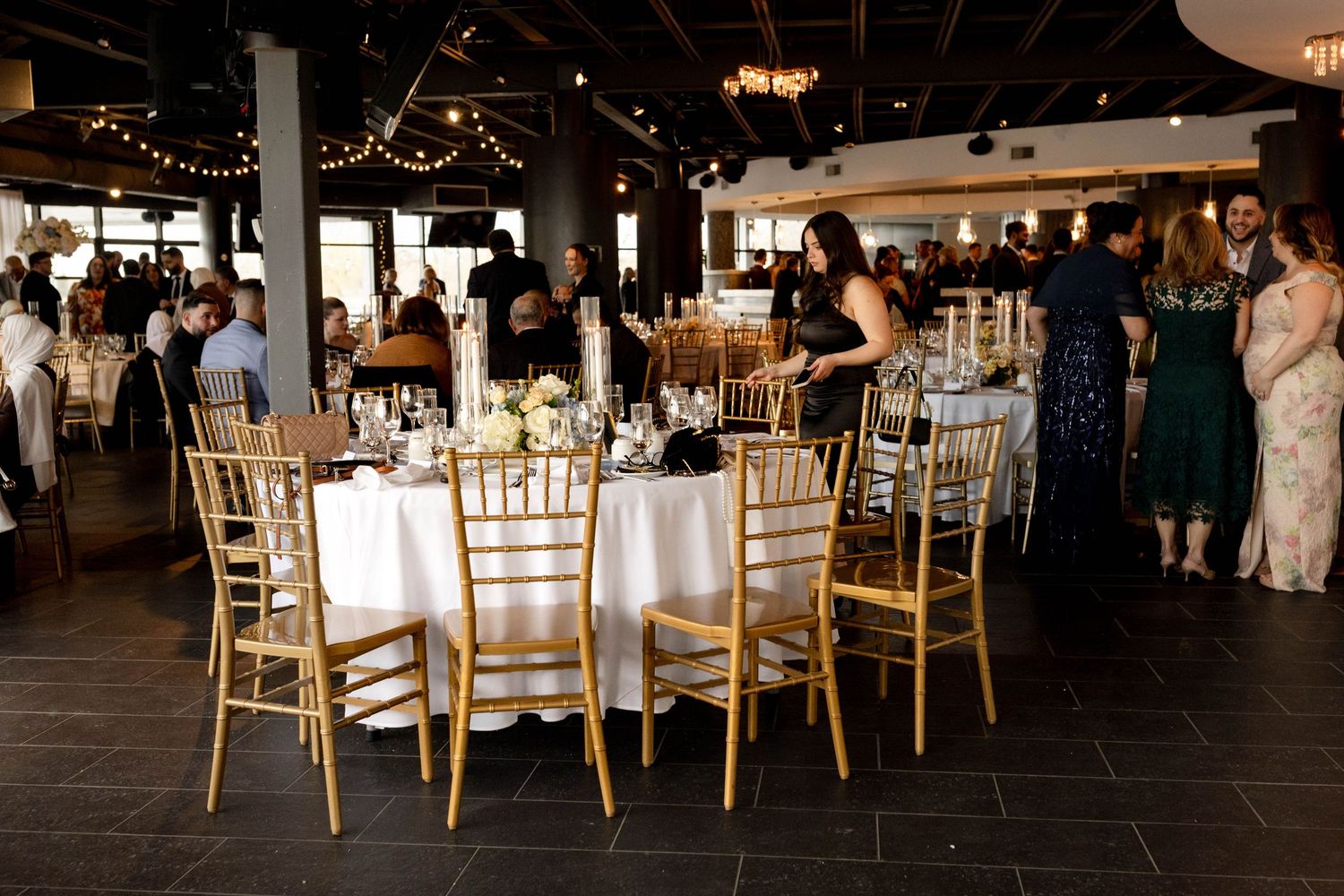 Elegant wedding reception with gold chiavari chairs, white tablecloths, and floral centerpieces in a modern venue.