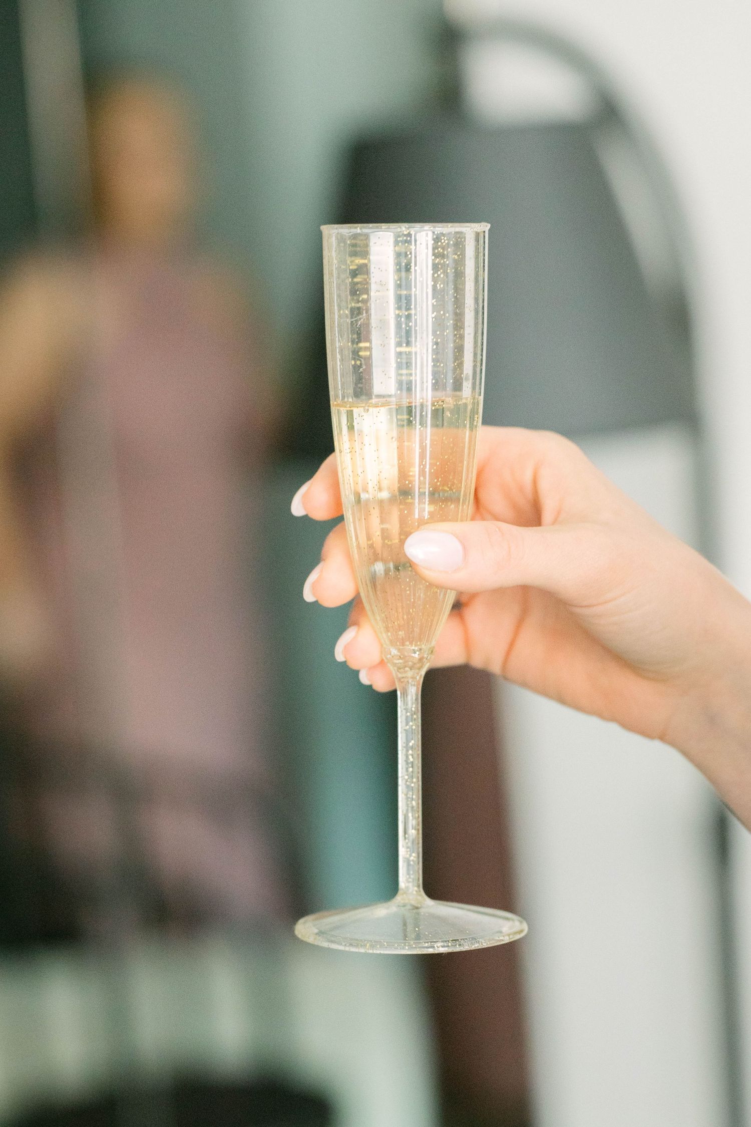 A woman's hand holding a clear champagne flute filled with sparkling wine at a celebration event.