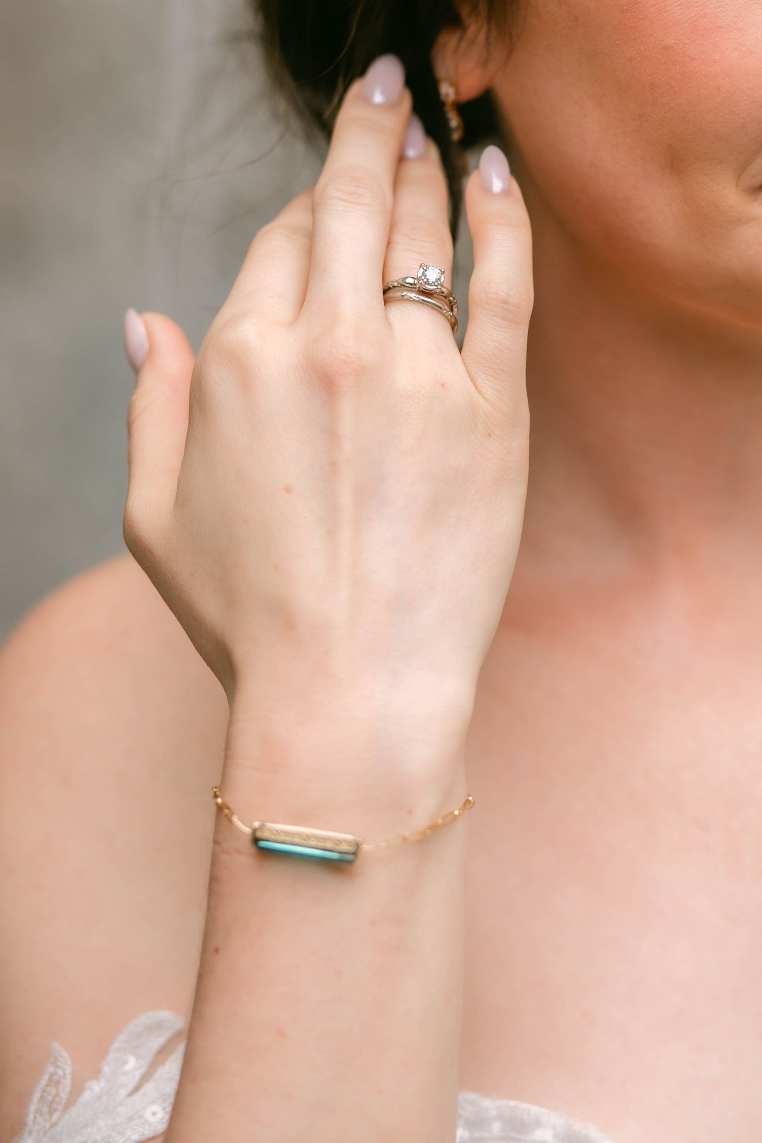Bride wearing a diamond engagement ring and gold bracelet with teal gemstone accent on her wrist.