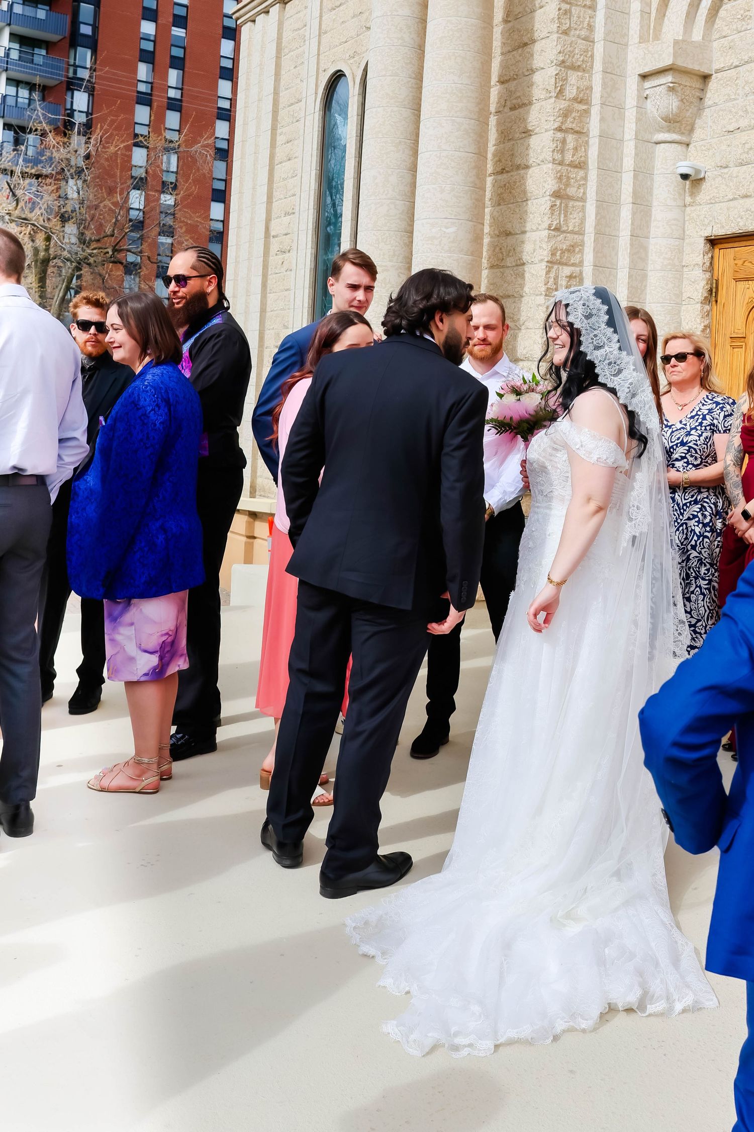Wedding guests line up outside a stone church building with white columns during a formal ceremony.
