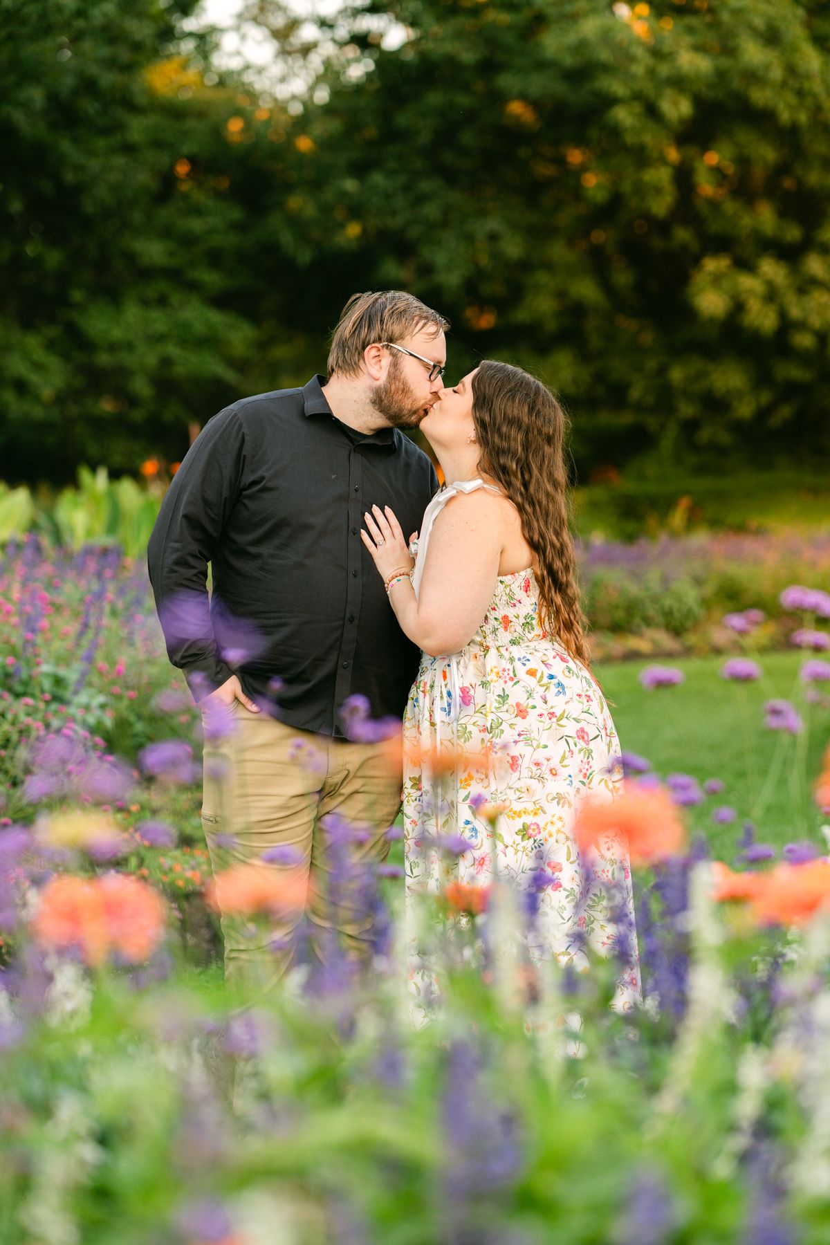 Couple sharing a romantic kiss surrounded by colorful purple and orange flowers in a lush garden setting.