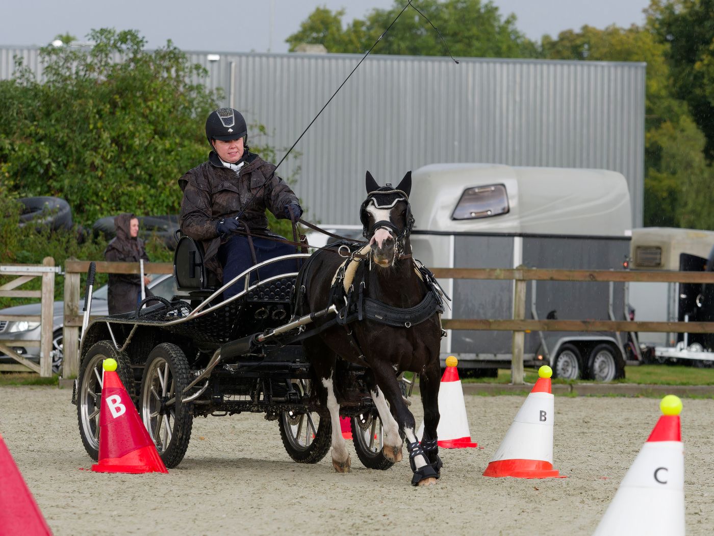 Horses and carriages navigate around orange cones in an outdoor equestrian competition course.