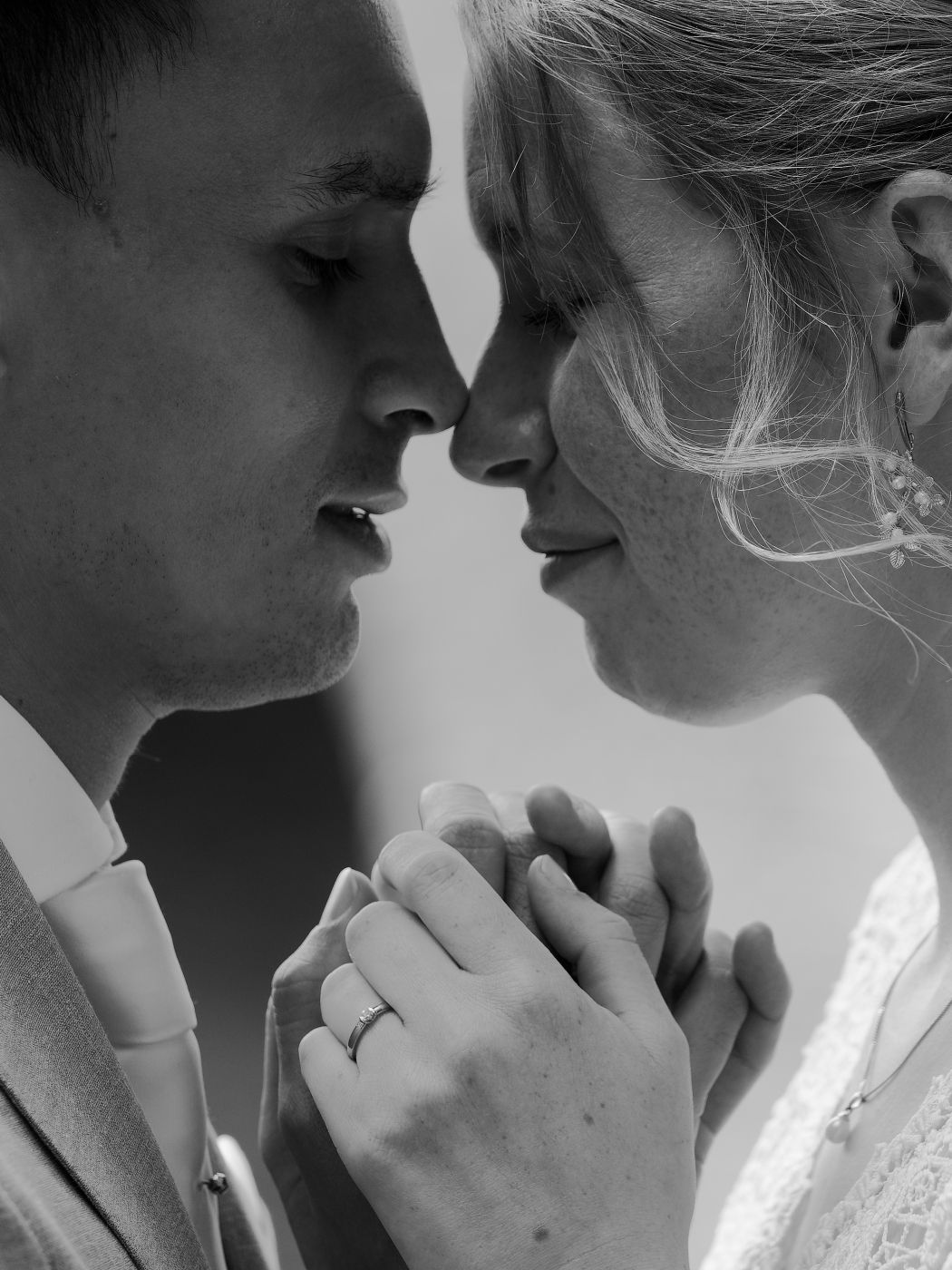 Black and white wedding photo of couple holding hands and touching foreheads, bride wearing engagement ring.