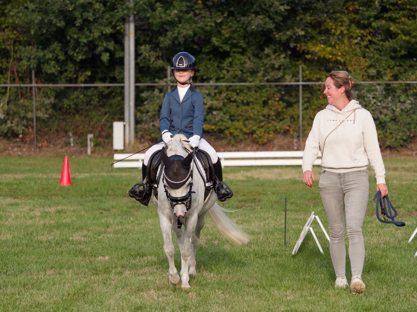 Small ponies and handlers navigate through a training course marked with red cones.