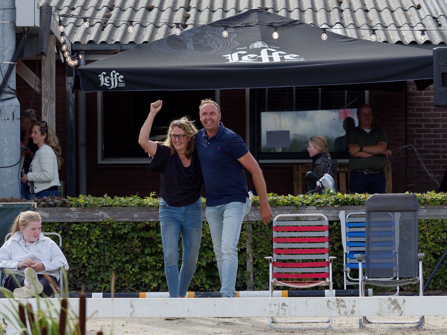 People gather under a covered viewing area to watch an equestrian presentation.