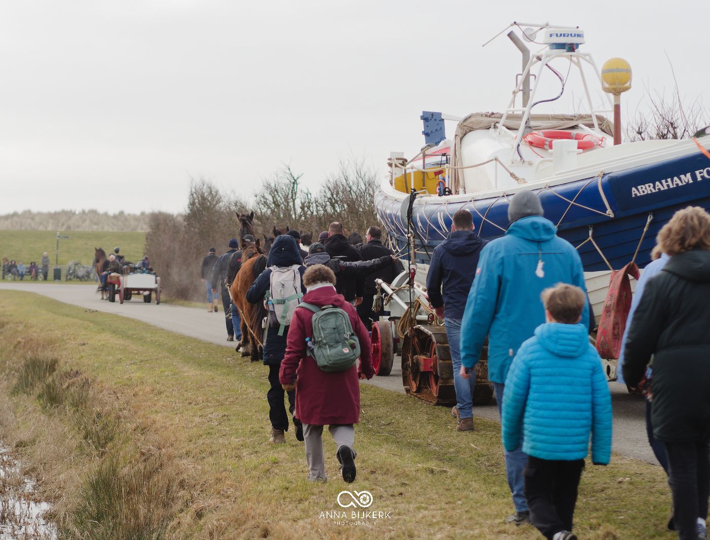 A line of people walking along a rural path during a group hiking event in winter weather conditions.